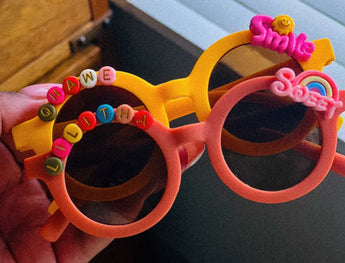 Colorful children's sunglasses with decorative elements held by a hand.