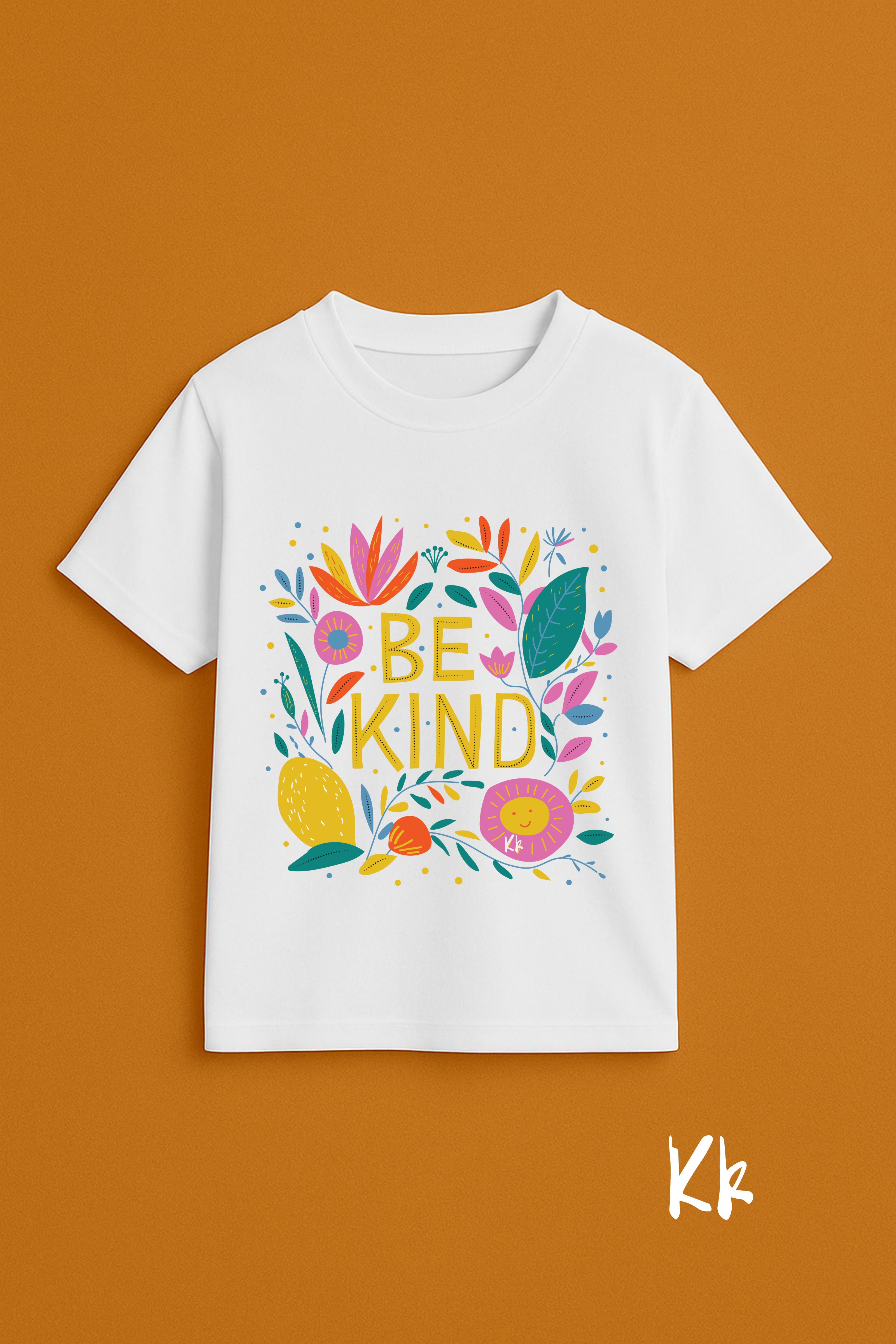 White t-shirt with colorful 'BE KIND' design on a brown background